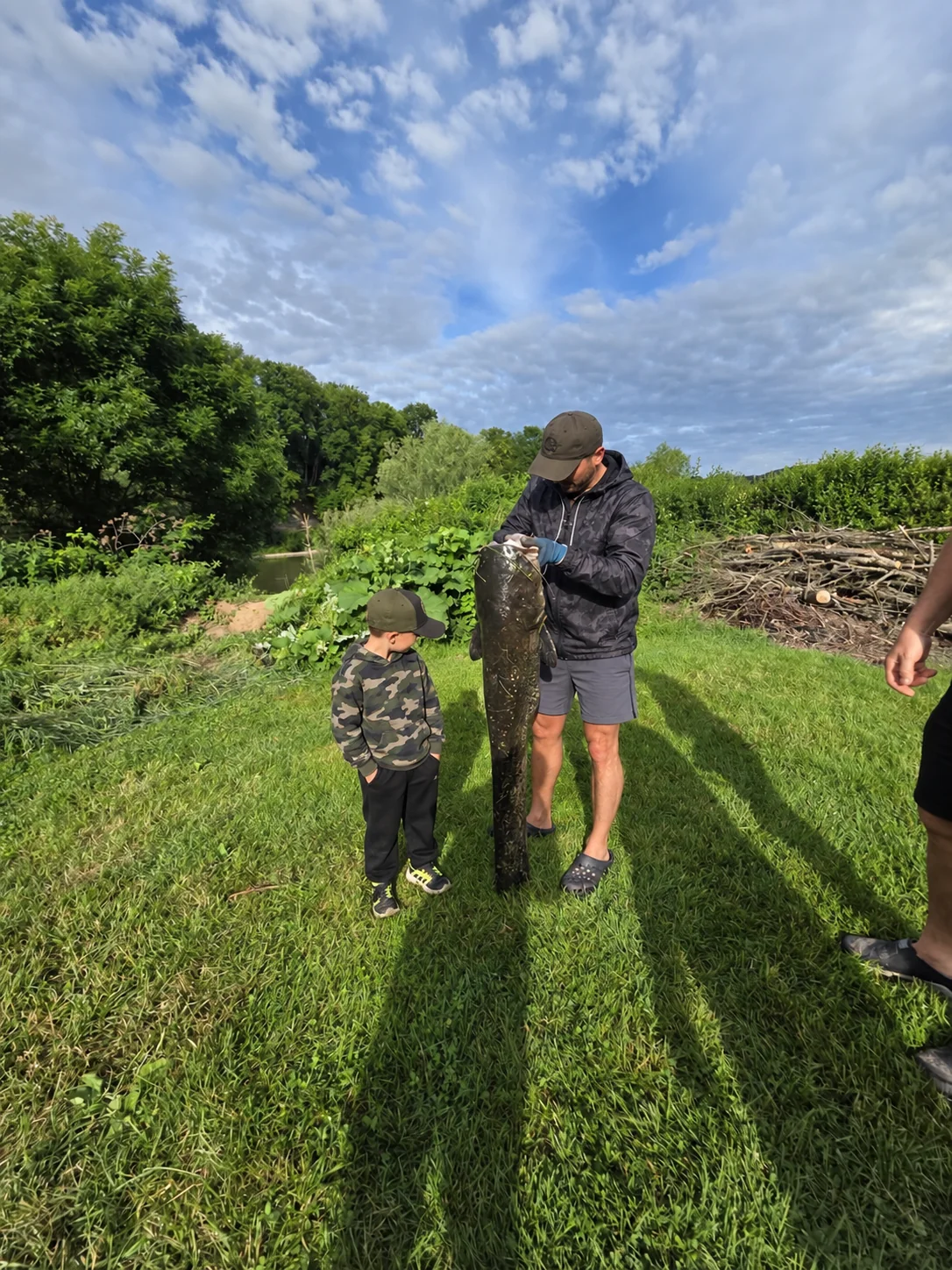 Angler mit einem Fisch und einem Kind auf der Wiese am Neckarufer