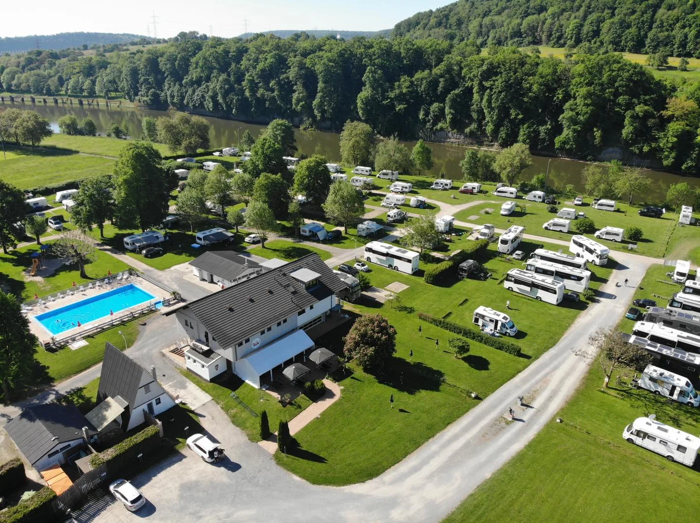 Luftaufnahme des Campingplatzes Cimbria mit Schwimmbecken, Bistrogebäude und Reihen von Stellplätzen, dahinter der Neckar