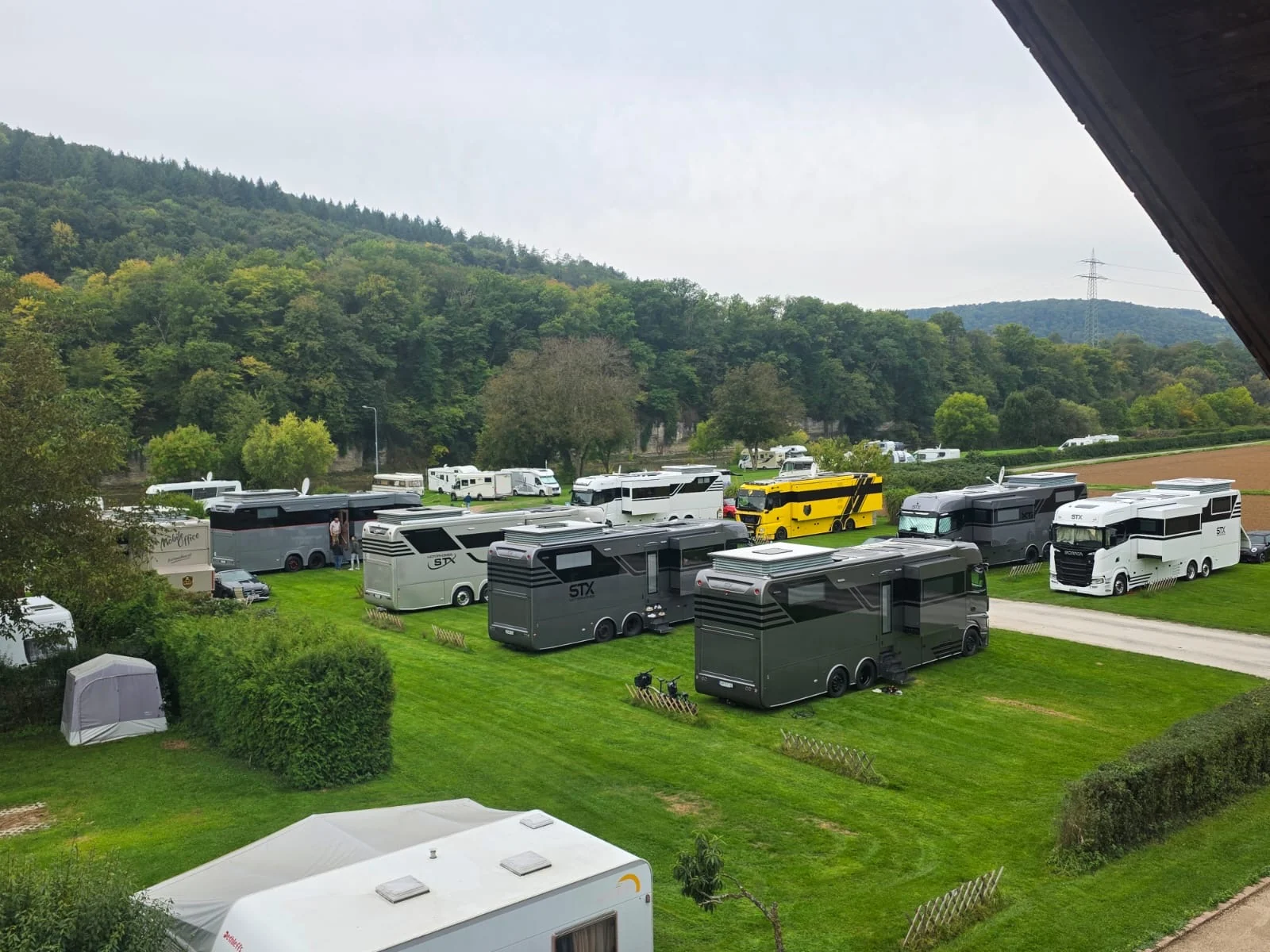 Wohnmobile und Wohnwagen auf grünen Stellplätzen des Campingplatzes vor bewaldeten Hügeln